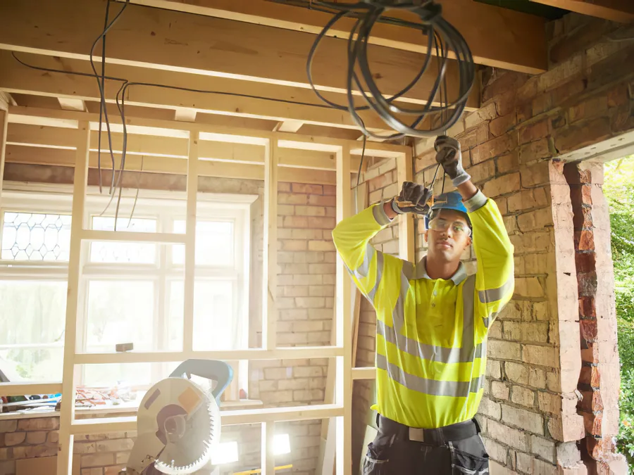 An electrician in hi-vis pulling wire through new framing