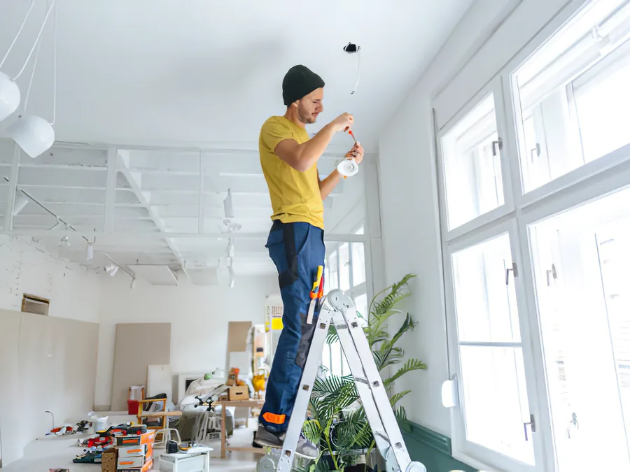 An electrician on a ladder fitting a ceiling light