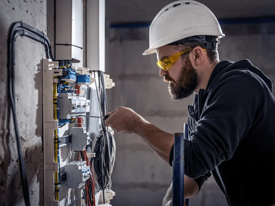An electrician in a hard hat working inside an electrical panel
