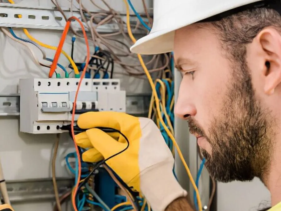 An electrician's gloved hands working on the wiring inside a breaker panel