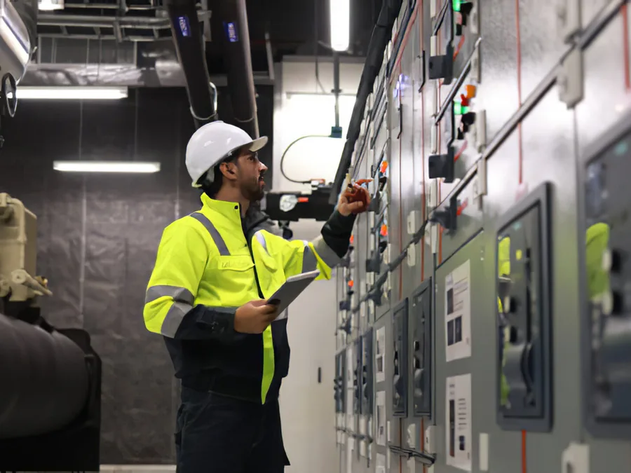 An electrician in hi-vis working in a commercial switchgear room